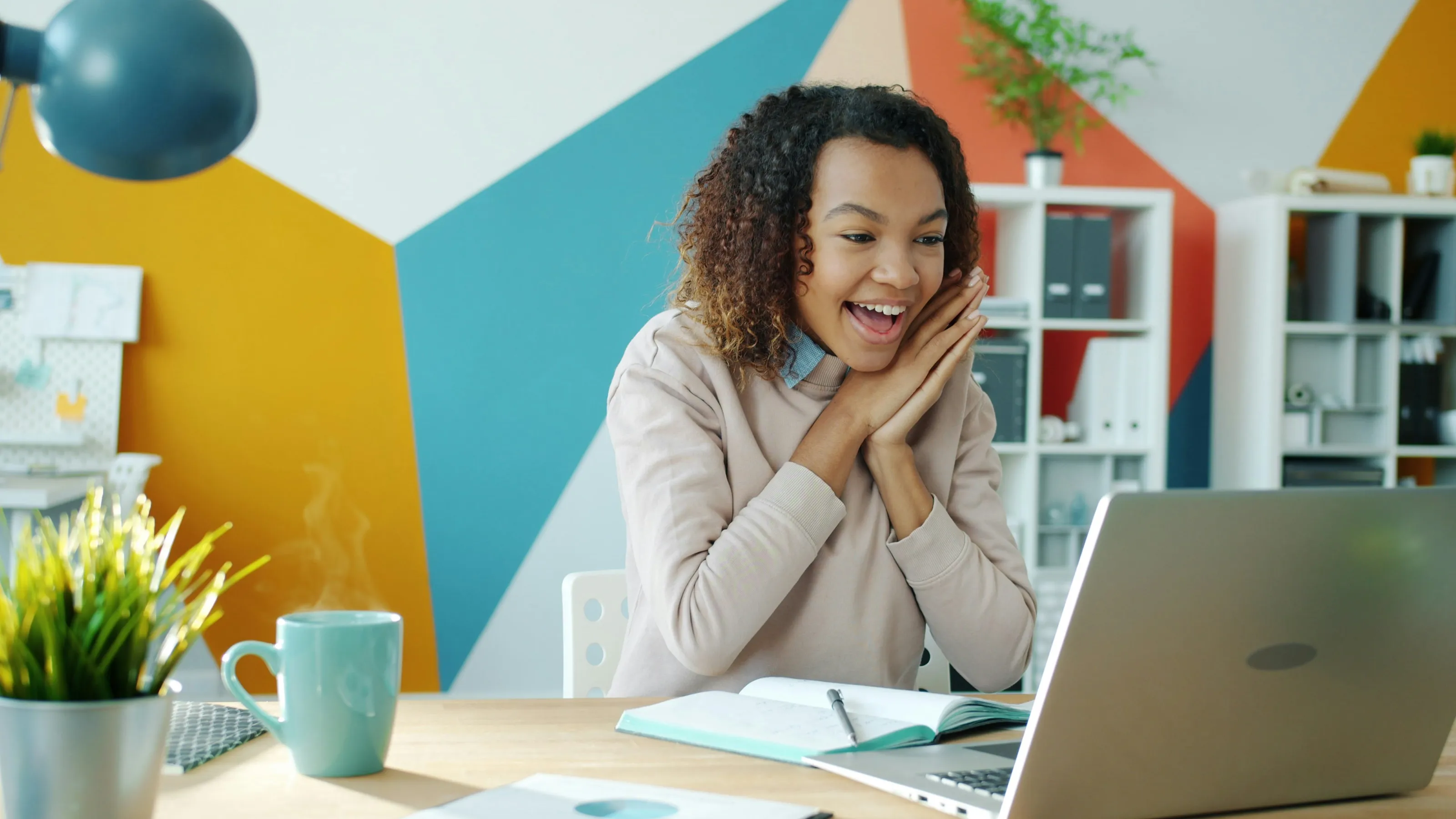 A woman smiling with delight at good news on her laptop